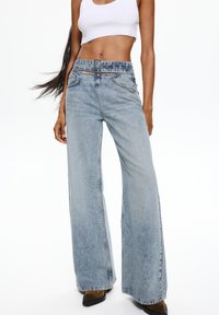 Light blue wide-leg denim jeans with a high-rise waist, belt loops, and subtle distressing. Finished with front pockets and a straight hem.