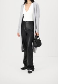 Světle šedý cardigan, bílý top s V výstřihem, černé kožené kalhoty, černá taška s textura vzorem a černé slip-on boty s akcenty.
