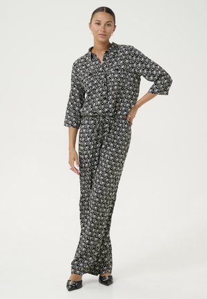 Combinaison à motifs noir et blanc avec une chemise à col et une taille cintrée, dotée de manches trois-quarts et de pantalons larges.