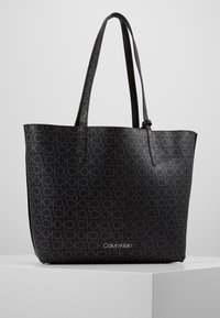 Černá taška na rameno s opakovaným vzorem loga Calvin Klein, plochý tvar, dvě dlouhé ucha a hladký textilní materiál.