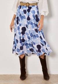 Blauwe en witte jurk met een patroon van lichtgewicht stof, met grote abstracte cirkels, plooien en een natural leren riem. Bruine suède laarzen maken de look compleet.
