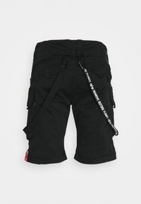 Short cargo noir avec plusieurs poches et une sangle noire et blanche portant la mention "REMOVE BEFORE FLIGHT" attachée à la taille.