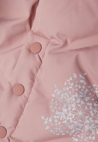 Rosa Steppjacke mit glatter Textur, ausgestattet mit runden rosa Knöpfen und einem weißen Blumenmuster-Design auf der linken Seite.