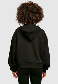 Sudadera negra de gran tamaño con capucha ajustable, puños acanalados y un acabado texturizado. La parte trasera presenta un diseño minimalista sin logotipos.