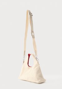 Geantă de umăr din țesătură crem cu căptușeală interioară roșie și curea bej ajustabilă cu cleme argintii, pe fundal alb.