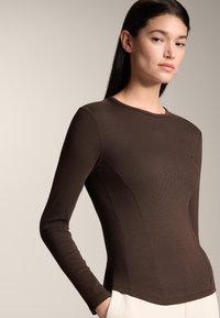 Brown long-sleeve top with a ribbed texture, fitted design, and a round neckline. Features subtle seams and a straight hem.