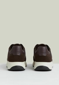 Tumed pruunid spordijalatsid, mis on valmistatud kombineeritud nubukist ja võrgust, kontrastse valge keskosa ja musta kummist välisküljega. Logo kandadel.