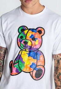 Camiseta blanca con un gráfico de un oso hecho de formas de ositos de goma en colores del arcoíris, con un contorno negro que resalta su diseño.