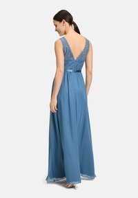 Vestito lungo blu da sera con un corpetto in pizzo e design a V sulla schiena. Realizzato in tessuto leggero con una gonna fluida e un dettaglio in vita.