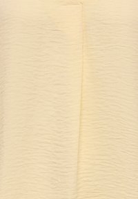 Gestructureerde lichtgele stof met een gekreukelde afwerking, voorzien van subtiele plooien en naden, wat een zachte, gelaagde uitstraling geeft.