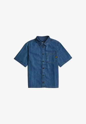 Chemise en denim à manches courtes, boutonnée, avec col et poche poitrine ornée d'une petite étiquette noire et jaune sur fond blanc.