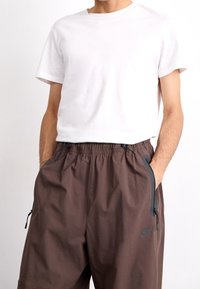 Vit kortärmad T-shirt kombinerad med lösa, bruna shorts med elastisk midja, sidofickor och en Nike-logga på benet.