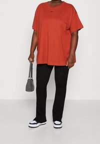 Överdimensionerad orange bomulls-t-shirt med en liten svart logotyp, matchad med svarta ribbade byxor och vita sneakers med blå accenter. Liten grå väska.