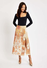 Black long-sleeve bodysuit paired with a patterned maxi skirt featuring swirls in orange and beige, split design, and metallic heels.