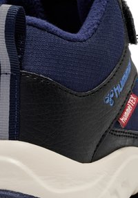 Marineblaue und schwarze Sneaker mit weißer Sohle, aus Textil- und Leder-Materialien, mit "hummel" und "hummel TEX" Logos an der Seite.