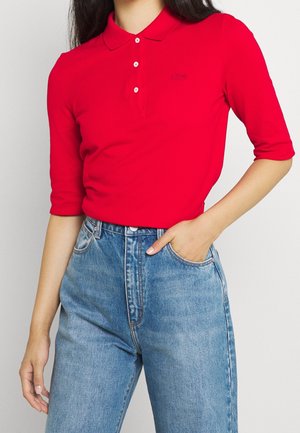 Rode poloshirt met een kraag, drie knopen en korte mouwen, gecombineerd met hoge lichtblauwe denim jeans. Subtiele logo-detail op de poloshirt.