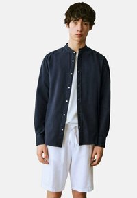 Mörkblå skjorta med ståkrage, långa ärmar och vita knappar, i kombination med vita shorts. Enkel, slät textur.