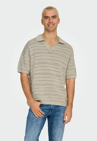 Lichtbeige gebreide polo met korte mouwen, voorzien van een textuurpatroon en een kraaglijn, gecombineerd met blauwe jeans.