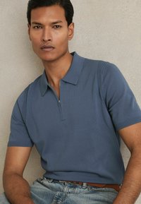 Polo dintr-o nuanță de albastru ardezie, cu fermoar pe jumătate și accente ribbate pe mâneci. Purtați cu blugi denim de un albastru deschis și o curea maro.