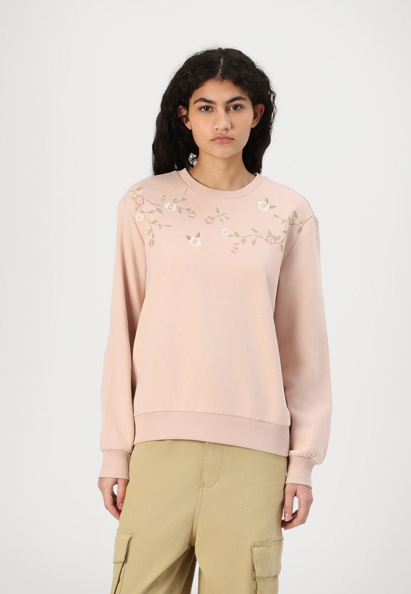 Rosa hettegenser med blomsterbroderi i rosa og grønt, ribbestrikket rund hals og lange ermer. Stoffet har en myk tekstur og en avslappet passform.