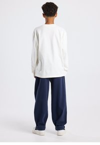 Long-sleeve white cotton shirt paired with navy blue wide-leg pants and white sneakers, featuring a relaxed fit and ribbed crew neckline.