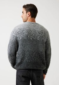 Maglione a maglia con gradiente grigio e una finitura morbida e testurizzata. Presenta un collo rotondo e una vestibilità rilassata. Indossato con jeans scuri.