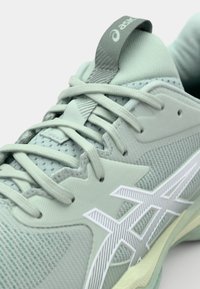 Chaussure de sport vert clair avec une tige en mesh respirant, des accents blancs, des lacets visibles et une semelle texturée. Présente un logo ASICS sur l'étiquette.
