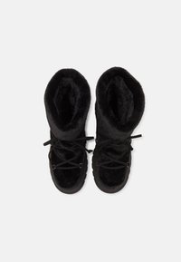 Une paire de bottes d'hiver en fourrure noire, avec des lacets, vues du dessus sur un fond blanc uni.