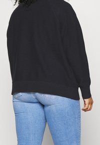 Schwarzer Pullover mit lockerer Passform, gestrickter Textur, geripptem Saum und langen Ärmeln, kombiniert mit hellblauen Denim-Jeans mit Gesäßtaschen.