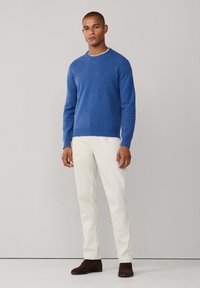 Blå stickad tröja med rund halsringning, i kombination med krämfärgade byxor och mörkbruna skor. Slät textur och figurnära design.