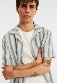 Korte mouw blouse met verticale zwart-witte strepen, gemaakt van een lichte stof, met een puntig kraag en knopen.