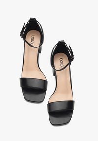 Black high-heeled sandals with a smooth faux leather upper, square toe, wide front strap, and adjustable ankle strap. Notable neutral insole.