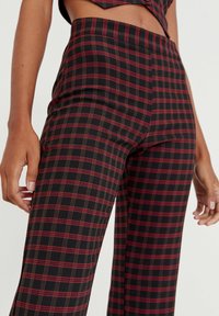 Pantaloni a quadri neri con linee rosse e verdi, design a vita alta, vestibilità strutturata, superficie del tessuto liscia e fascia minimalista in vita.