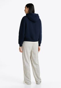 Granatowa bluza z kapturem, z kieszenią kangurzą i sznurkiem, zestawiona z kremowymi spodniami z pionowymi, wielokolorowymi paskami.
