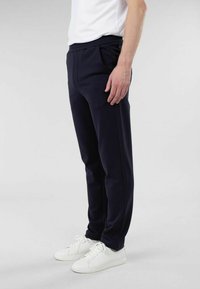 Marineblå joggebukser med elastisk midje, sidelommer, avsmalnede bein og en glatt stofffinish, og kombinert med hvite joggesko.