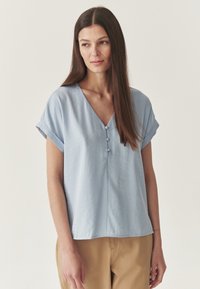 Blusa azzurro chiaro a maniche corte con scollo a V, caratterizzata da tre bottoni sul davanti, realizzata in un tessuto morbido e testurizzato.
