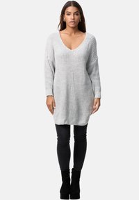 Suéter de punto gris claro, oversized, con un profundo escote en V, textura acanalada, mangas largas, combinado con jeans ajustados oscuros y botas de tobillo con tacón.