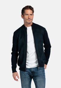 Marine bomberjack met een suède lichaam en gebreide mouwen, voorzien van een rits aan de voorkant en een geribde kraag, gecombineerd met een wit T-shirt en jeans.