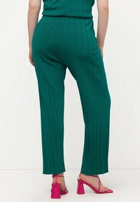 Pantalones de pierna ancha de canalé en color teal, confeccionados en material ligero, combinados con sandalias de tacón cuadrado rosas con correas en el tobillo.