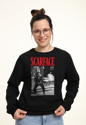Felpa nera con un'immagine grande in bianco e nero di un personaggio con una pistola, incorniciata da testo rosso che legge "SCARFACE."