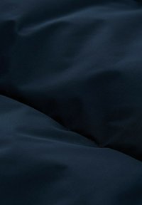 Námornícky modrý textil so hladkou, mierne matnou textúrou, vykazujúci jemné záhyby a vrásky, ktoré vytvárajú vizuálnu hĺbku a rozmer.