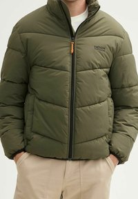 Oliven grøn pufferjakke med horisontal syning, sort lynlås og orange trækkappe. Har en høj krave og sidelommer.