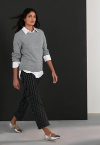 Pulover gri peste o cămașă albă cu guler, asortat cu pantaloni negri cu buline și pantofi plate argintii. Design simplu și modern, cu culori contrastante.