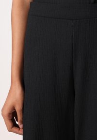 Black trousers feature a textured fabric with a subtle vertical pattern. The waistband is neatly finished, complementing the overall design.