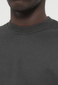 Σκούρο γκρι φούτερ με ριμπ λαιμόκοψη και υφή υφάσματος. Στο κοντινό πλάνο φαίνεται το λείο υλικό με διακριτικές λεπτομέρειες ραφών.