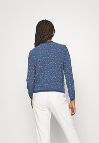 Blå sweatshirt med blommönster och långa ärmar, ribbade ärmslut och halsringning, tillverkad av mjukt tyg. Bärs med vita byxor.