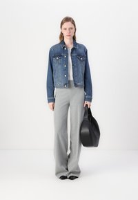 Denim jacket with two chest pockets, light blue color. Grey wide-leg pants and black handbag. Flat black shoes complete the outfit.