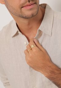 Lichtbeige linnen overhemd met een kraag en parelmoer knopen. Hand versierd met twee gouden ringen, één rond en één eenvoudige band.