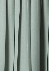 Tela plisada en un suave tono verde apagado, mostrando una superficie texturizada con patrones sutiles, dispuesta en pliegues verticales.