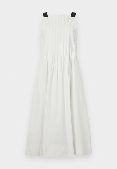 Weißes ärmelloses Kleid mit schwarzen Schulterträgern, das vertikale Falten auf dem Oberteil und einen ausgestellten Rock aufweist. Glatte Stofftextur.